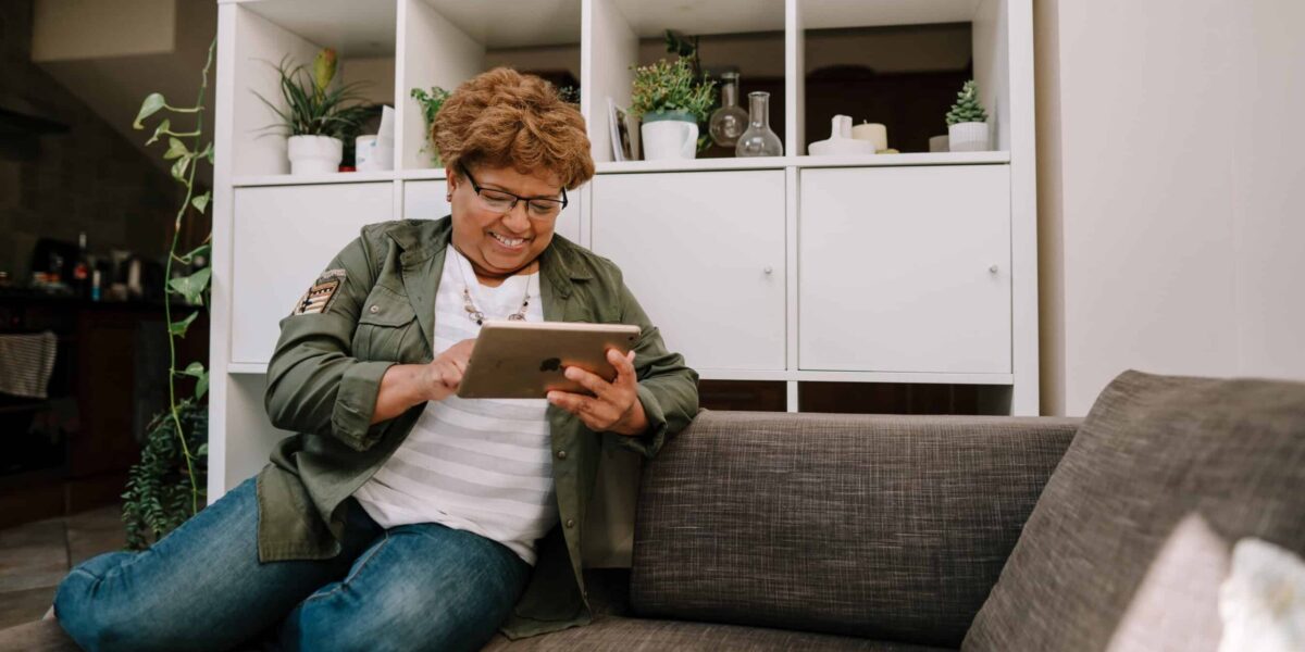 Woman sits on sofa smiling at her ipad