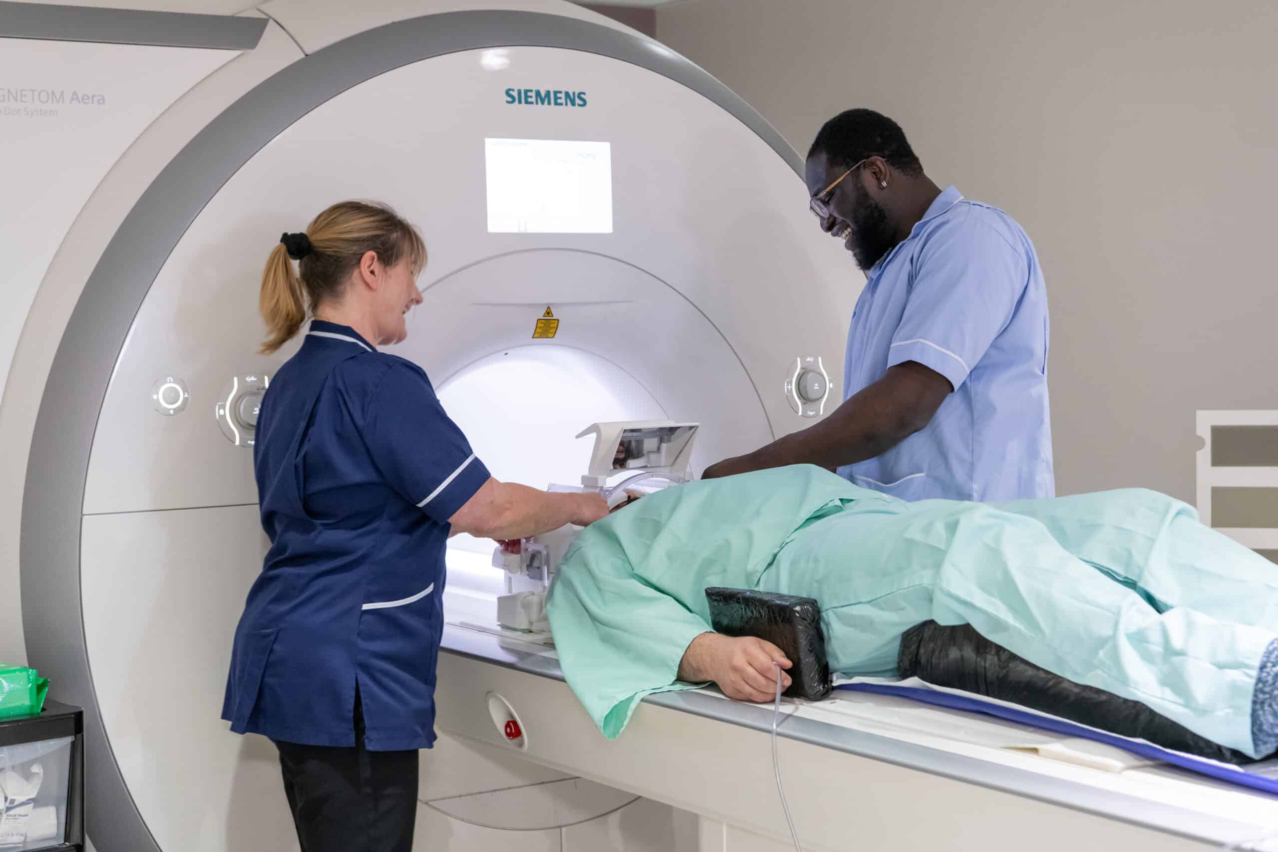 A man lies on a bed about to enter a MRI scanner with two nurses above him