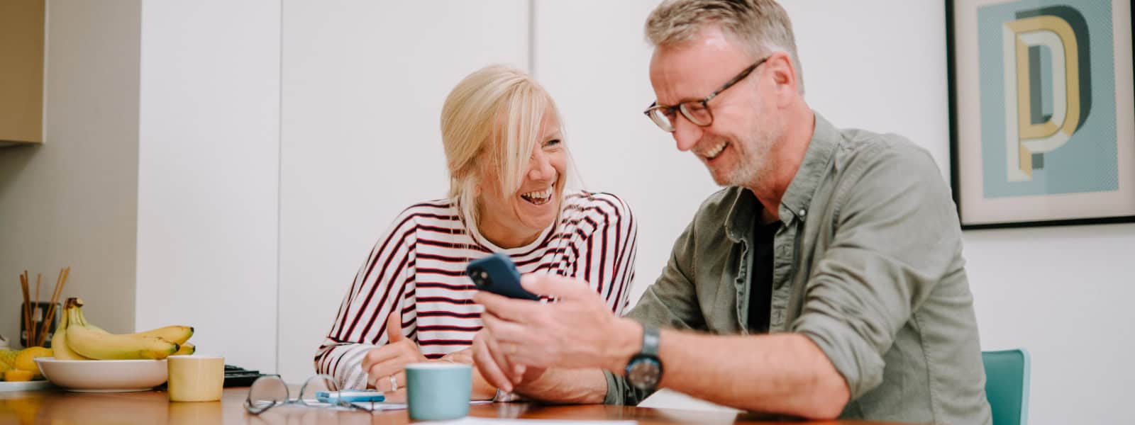 Two people smile and laugh together whilst looking at a phone