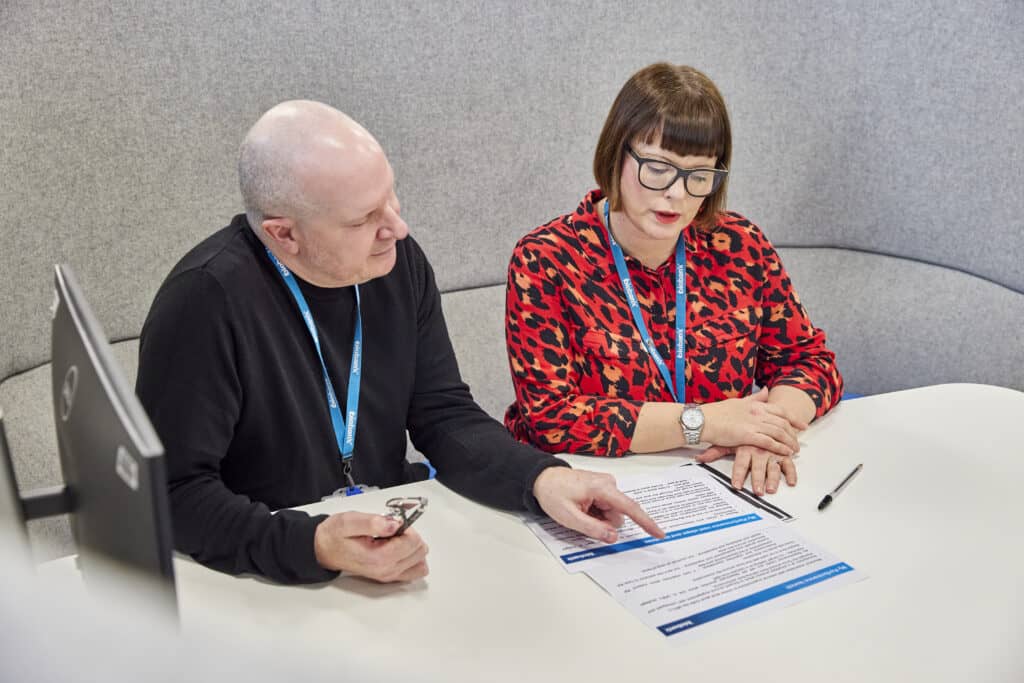 two staff members discuss documents laid out on a desk