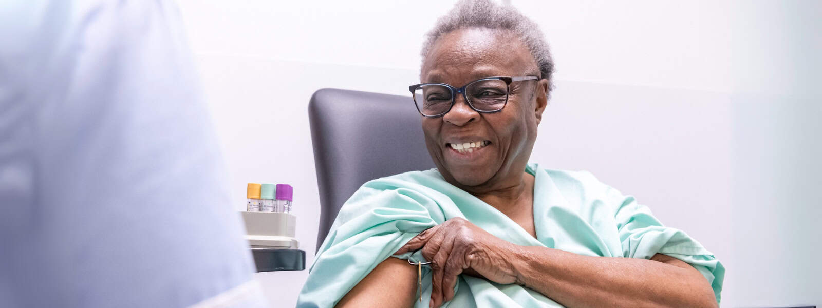 Lady smiling and pulling up the sleeve of her hospital gown, about to have her blood taken
