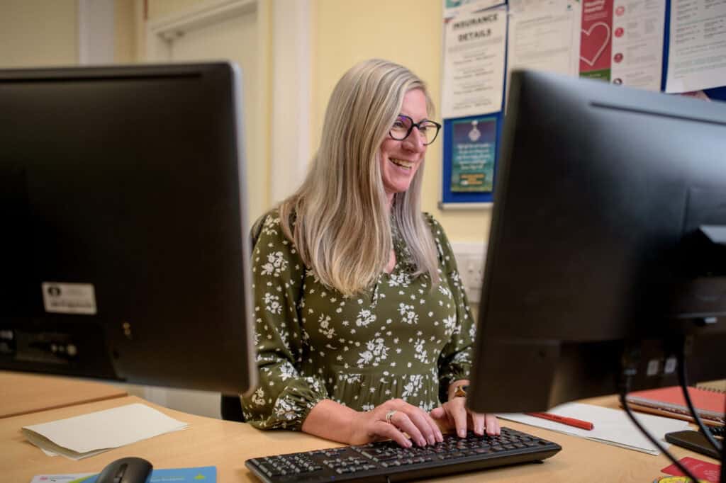 A woman on a computer at work smiles whilst looking at the screen