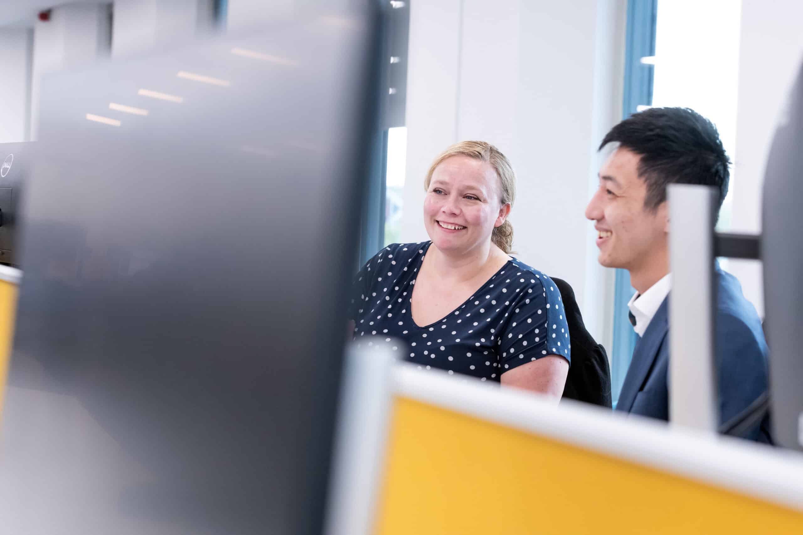 Two people sit in front of a computer screen smiling