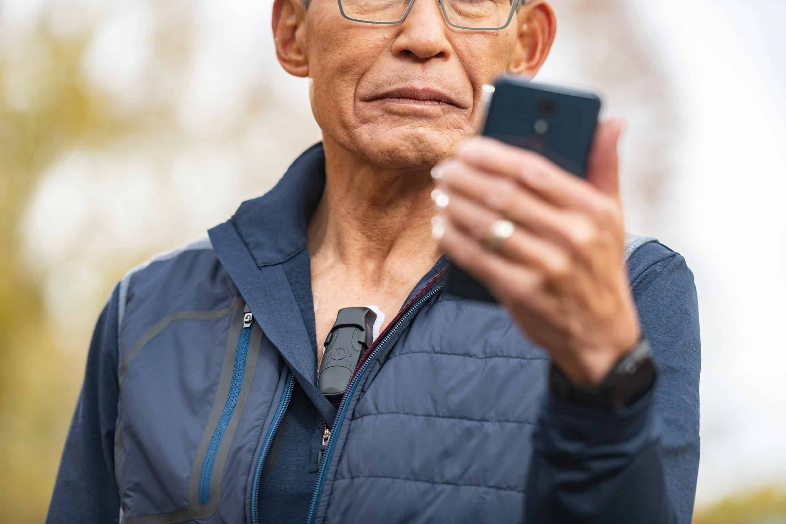 A person wears a heart monitor on their chest whilst looking at their phone