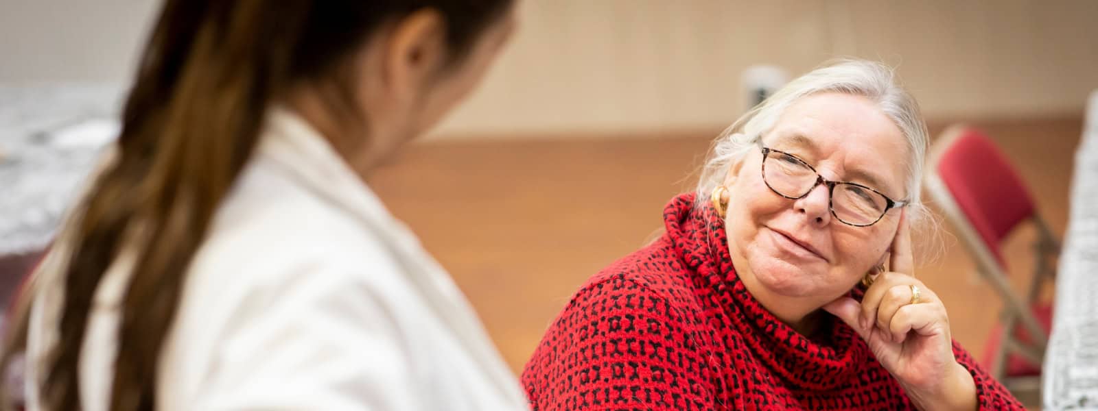 A woman rests her head on her hand, turning to look at another woman