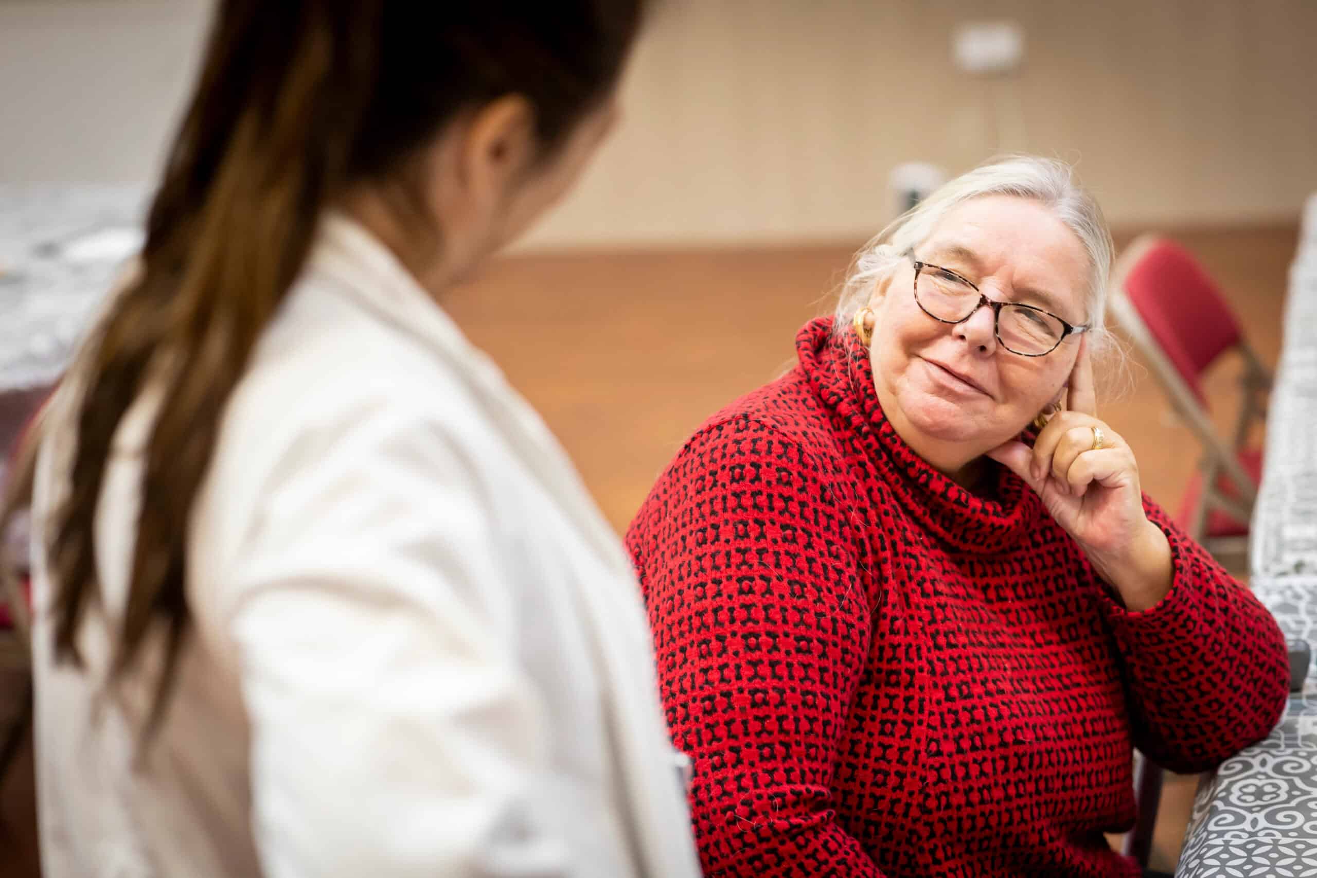 A woman rests her head on her fingers and turns to listen to someone.