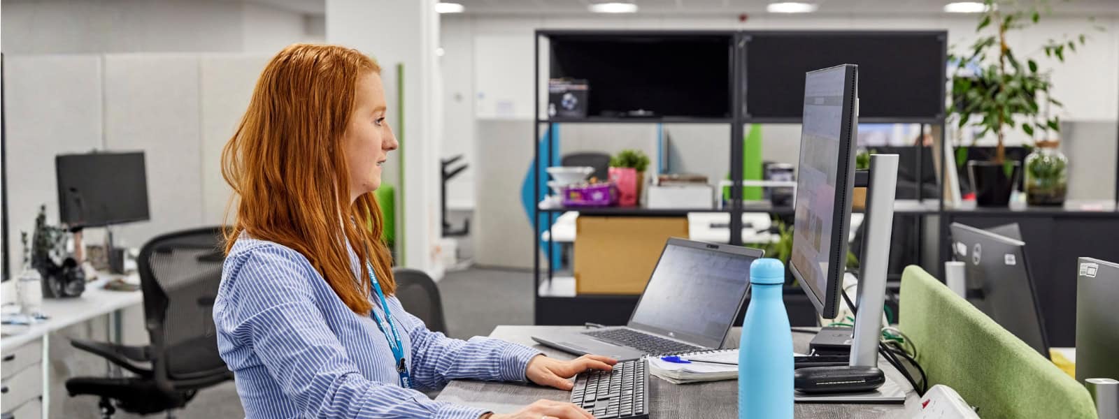 A woman works at a desk, looking at her monitor screen.